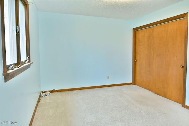 unfurnished bedroom featuring light carpet, a textured ceiling, and a closet