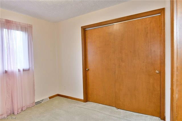 unfurnished bedroom featuring a closet, light colored carpet, and a textured ceiling