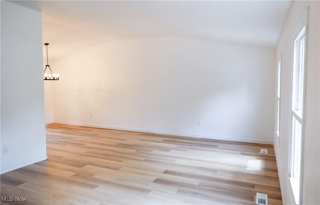 spare room with light hardwood / wood-style flooring, vaulted ceiling, and a notable chandelier