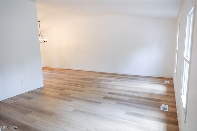 empty room featuring an inviting chandelier, light hardwood / wood-style flooring, and lofted ceiling