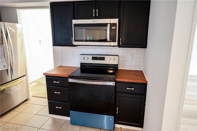 kitchen with stainless steel appliances, tasteful backsplash, butcher block counters, and light tile patterned flooring