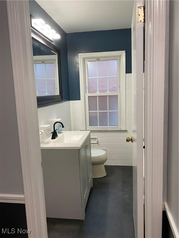 bathroom featuring vanity, concrete floors, tile walls, and toilet