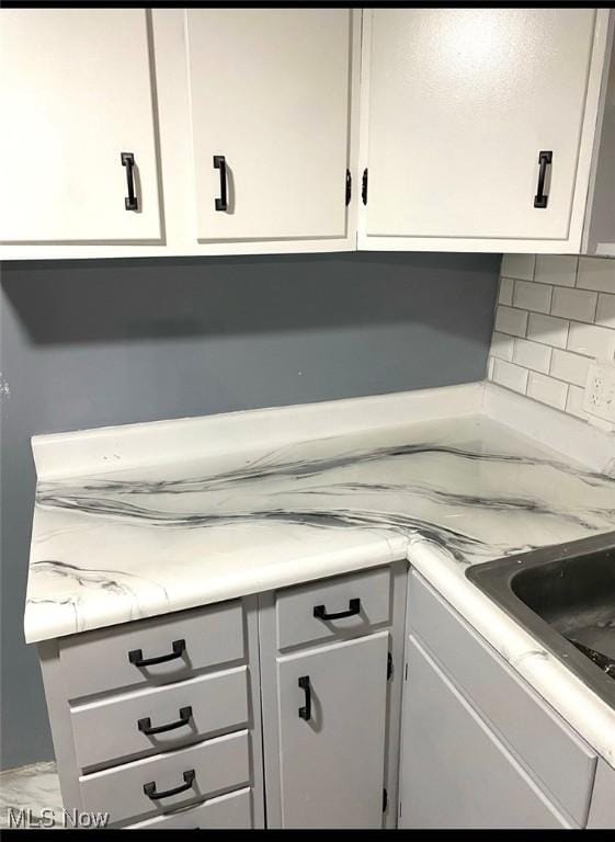 details with sink, white cabinetry, and backsplash