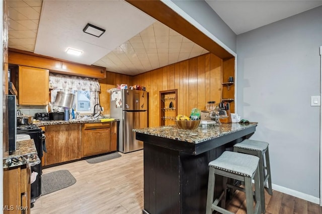 kitchen with dark stone counters, wooden walls, light hardwood / wood-style floors, kitchen peninsula, and stainless steel refrigerator