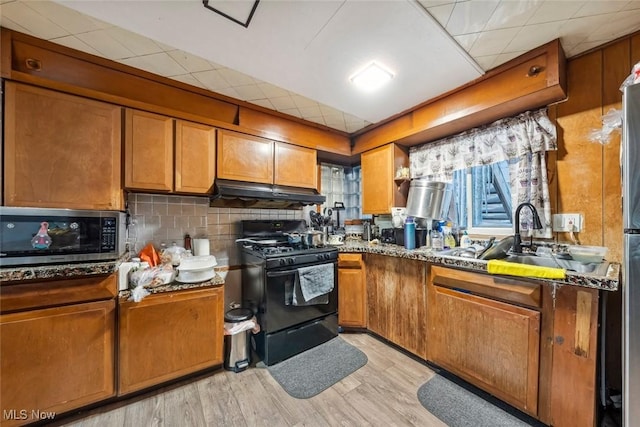 kitchen with a drop ceiling, dark stone counters, black range with gas stovetop, sink, and light hardwood / wood-style flooring