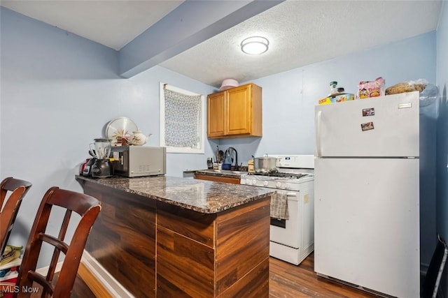 kitchen with white appliances, dark stone counters, sink, dark hardwood / wood-style floors, and a textured ceiling