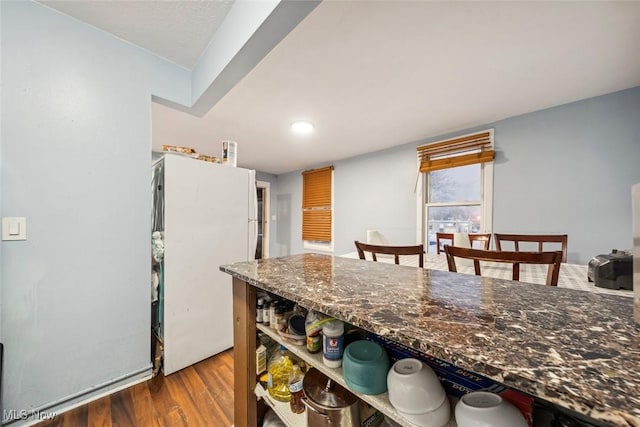 kitchen featuring wood-type flooring, white fridge, and dark stone counters