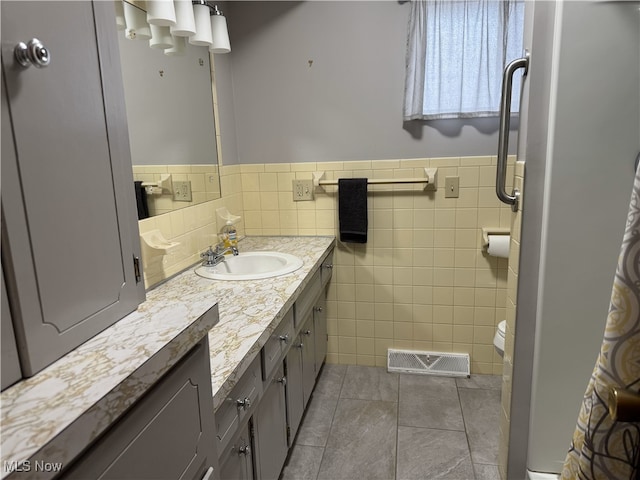 bathroom featuring tile patterned floors, vanity, toilet, and tile walls