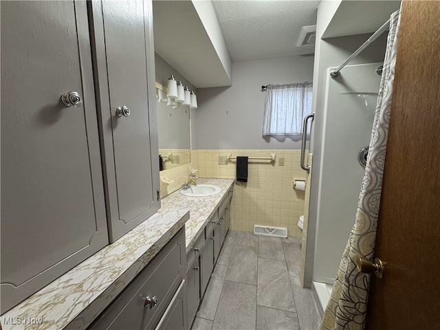 bathroom featuring tile patterned floors, a shower, a textured ceiling, vanity, and tile walls