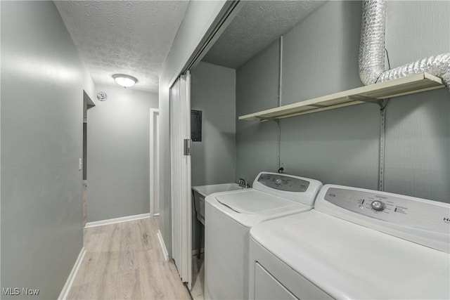 laundry room featuring a textured ceiling, light hardwood / wood-style floors, and washing machine and clothes dryer