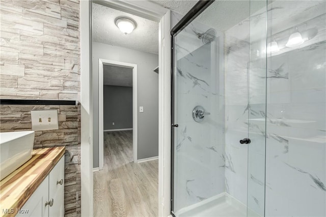 bathroom with a shower with shower door, wood-type flooring, a textured ceiling, and vanity