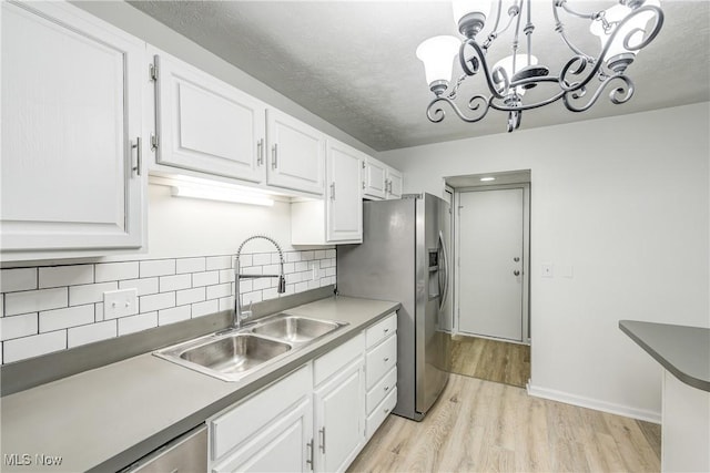 kitchen featuring backsplash, white cabinets, sink, hanging light fixtures, and light hardwood / wood-style floors