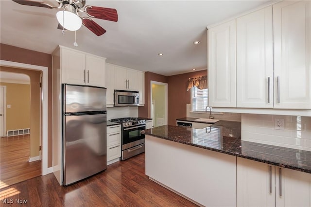 kitchen featuring dark hardwood / wood-style flooring, stainless steel appliances, sink, dark stone countertops, and white cabinetry