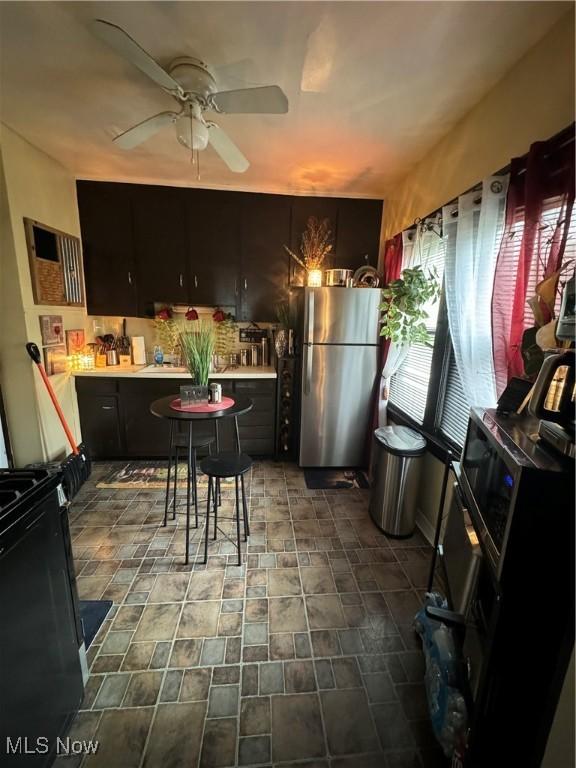 kitchen featuring ceiling fan, black electric range oven, dark brown cabinets, and stainless steel refrigerator