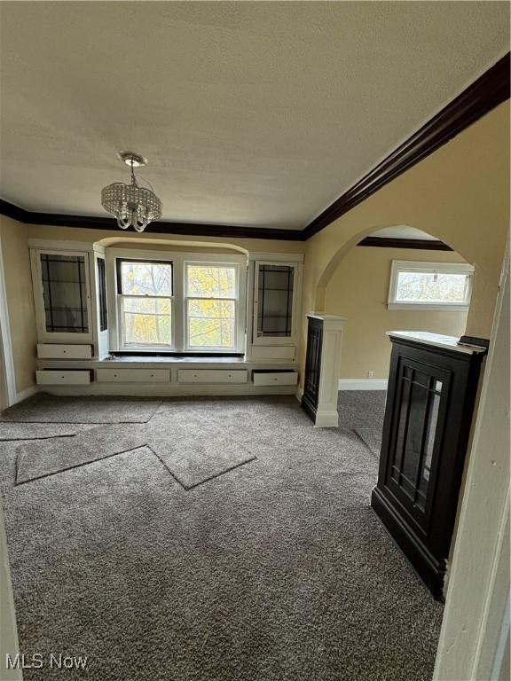 unfurnished living room featuring carpet, ornamental molding, a wealth of natural light, and a chandelier