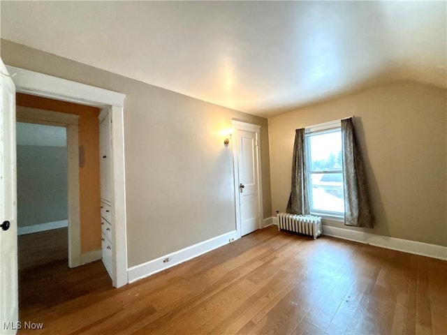 unfurnished room with hardwood / wood-style floors, lofted ceiling, and radiator