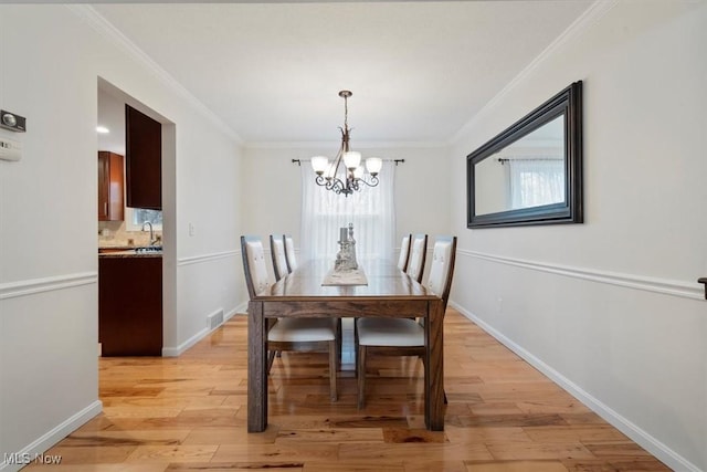 dining room with light hardwood / wood-style floors, an inviting chandelier, ornamental molding, and sink