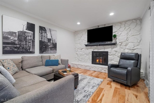 living room with a stone fireplace, crown molding, and hardwood / wood-style floors