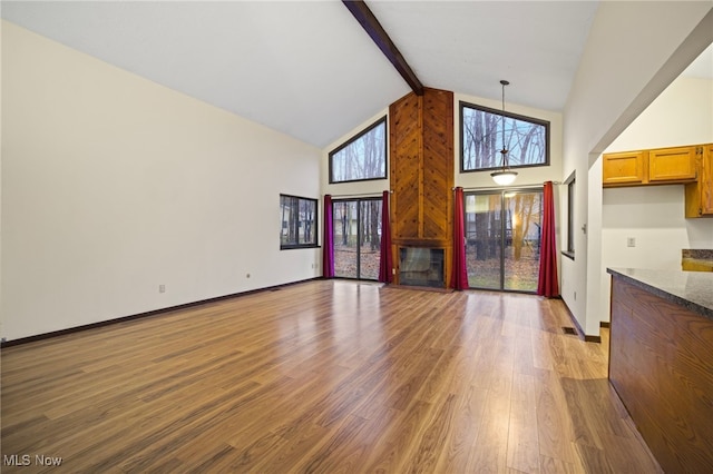 unfurnished living room with beamed ceiling, light wood-type flooring, and high vaulted ceiling