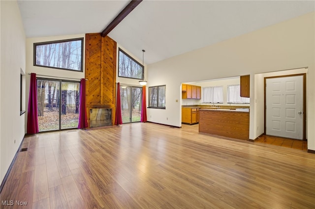 unfurnished living room with plenty of natural light, light hardwood / wood-style floors, beam ceiling, and high vaulted ceiling