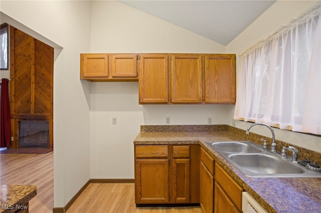 kitchen with dishwasher, sink, vaulted ceiling, and light wood-type flooring