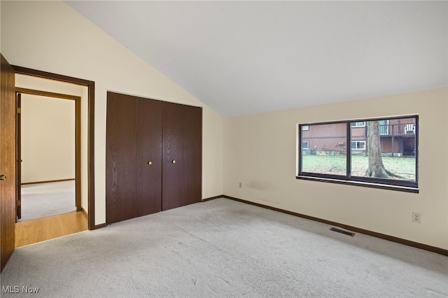 unfurnished bedroom featuring a closet, light colored carpet, and vaulted ceiling