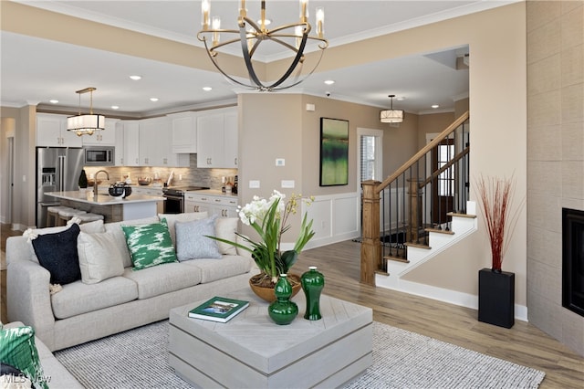 living room with a tile fireplace, sink, ornamental molding, and light wood-type flooring