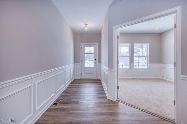 entryway with dark colored carpet, dark wood-type flooring, wainscoting, and visible vents