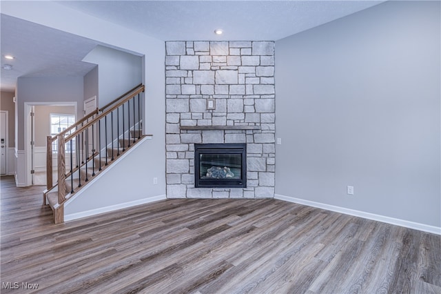 unfurnished living room featuring baseboards, a stone fireplace, stairway, and light wood-style floors