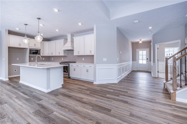 kitchen featuring an island with sink, appliances with stainless steel finishes, custom exhaust hood, light countertops, and white cabinetry