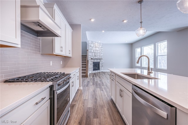 kitchen featuring hanging light fixtures, custom exhaust hood, stainless steel appliances, light countertops, and a sink