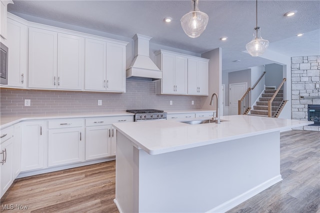 kitchen featuring stainless steel stove, light countertops, a sink, and premium range hood