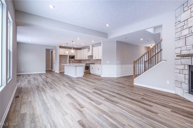 unfurnished living room featuring a fireplace, visible vents, a sink, light wood-type flooring, and stairs