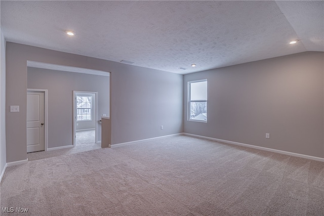 empty room featuring light carpet, baseboards, vaulted ceiling, a textured ceiling, and recessed lighting