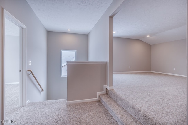 stairway featuring a textured ceiling, carpet, lofted ceiling, and baseboards