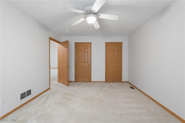 unfurnished bedroom with a textured ceiling, light colored carpet, and ceiling fan