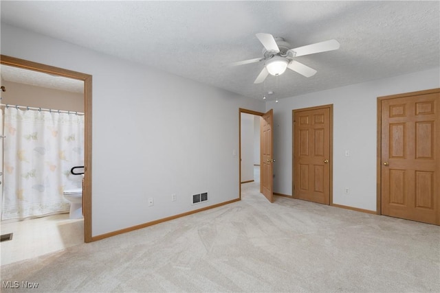 unfurnished bedroom with a textured ceiling, light colored carpet, ensuite bath, and ceiling fan