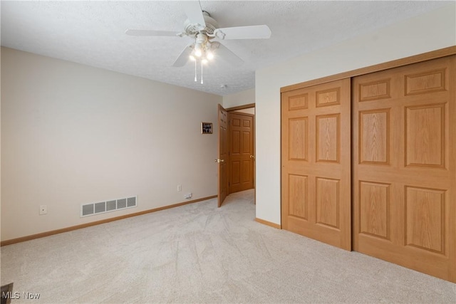 unfurnished bedroom with ceiling fan, a closet, light colored carpet, and a textured ceiling