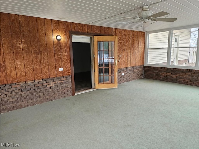 interior space with wood walls, ceiling fan, and brick wall