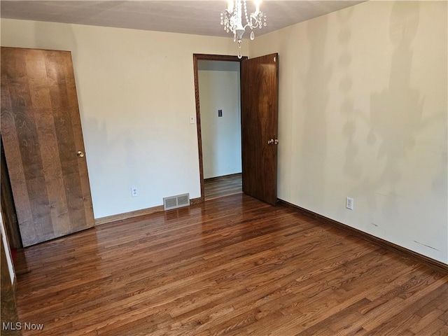 unfurnished room featuring dark wood-type flooring and an inviting chandelier