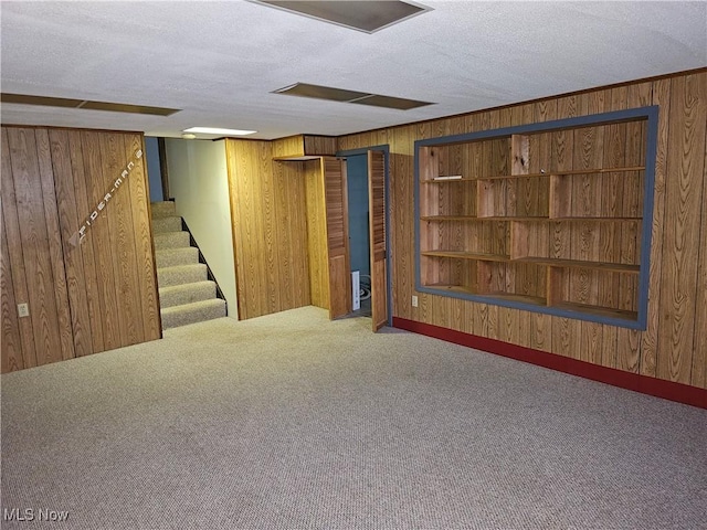 basement featuring carpet flooring, wood walls, and a textured ceiling