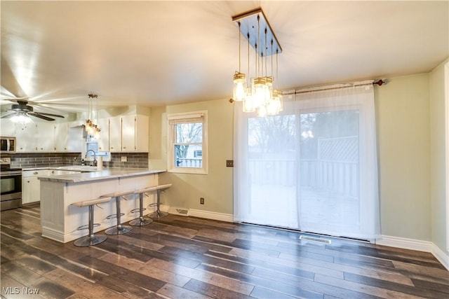 kitchen featuring stainless steel appliances, white cabinetry, a kitchen bar, tasteful backsplash, and kitchen peninsula