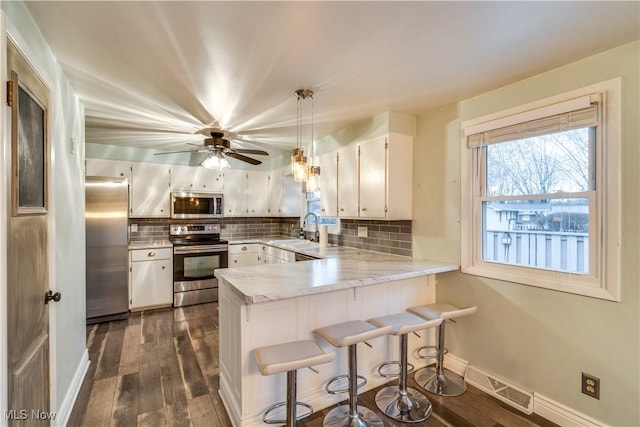 kitchen featuring stainless steel appliances, kitchen peninsula, sink, white cabinetry, and decorative light fixtures