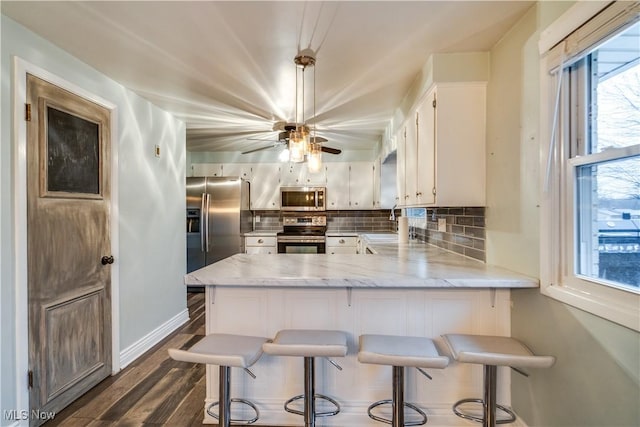 kitchen with stainless steel appliances, a breakfast bar area, white cabinets, and kitchen peninsula