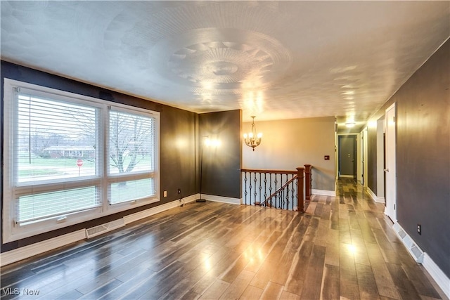 empty room with dark hardwood / wood-style flooring and a chandelier