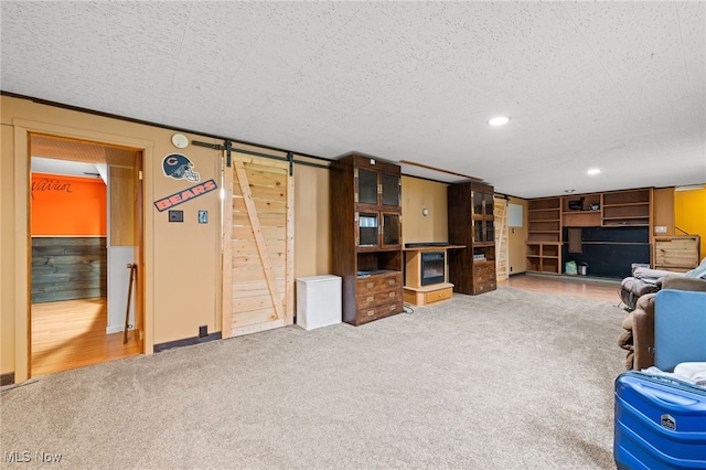 carpeted living room featuring wood walls, a barn door, and a textured ceiling