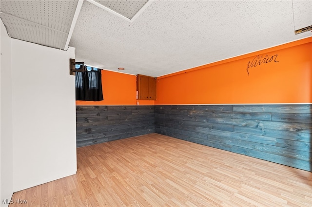 unfurnished room featuring wooden walls, light hardwood / wood-style flooring, and a textured ceiling