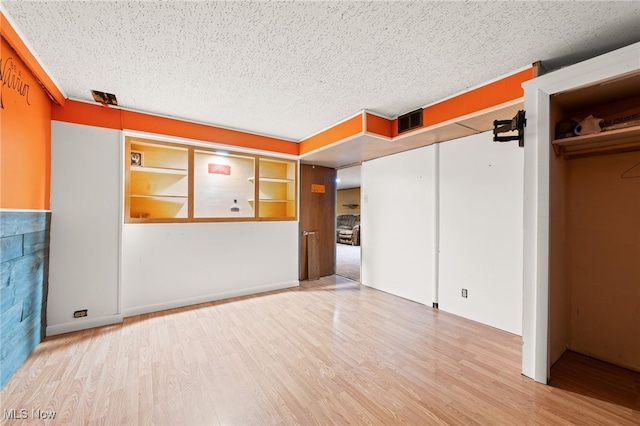 unfurnished living room featuring wood-type flooring, a textured ceiling, and built in shelves