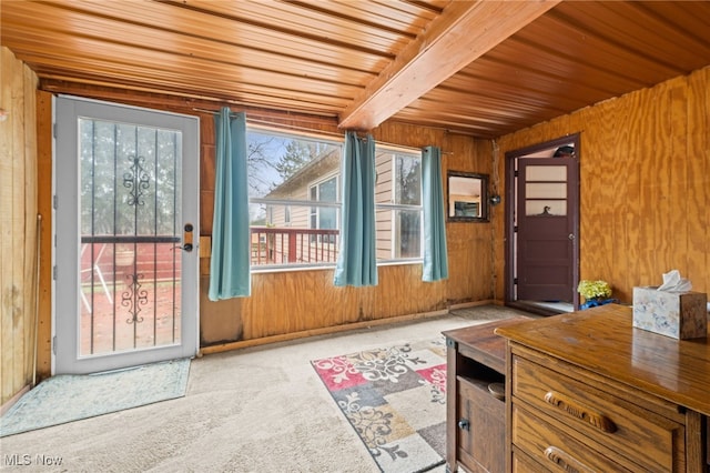 doorway with beamed ceiling, wood walls, light colored carpet, and wooden ceiling