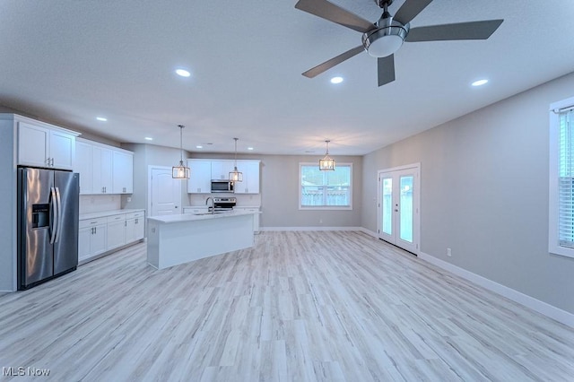 kitchen with white cabinetry, stainless steel appliances, light hardwood / wood-style flooring, decorative light fixtures, and a center island with sink